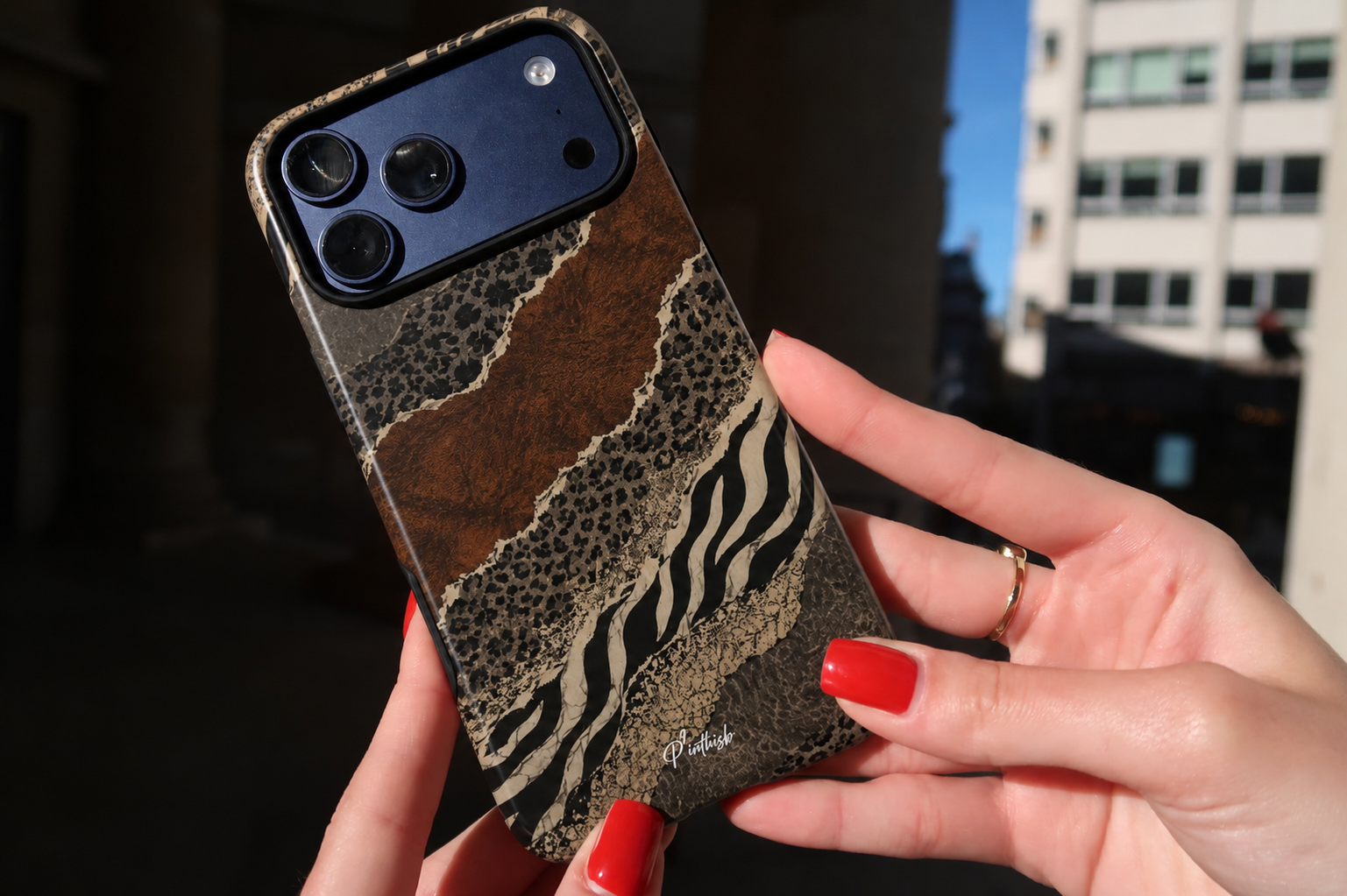 Hand holding a phone case with animal print design against a blurred cityscape background